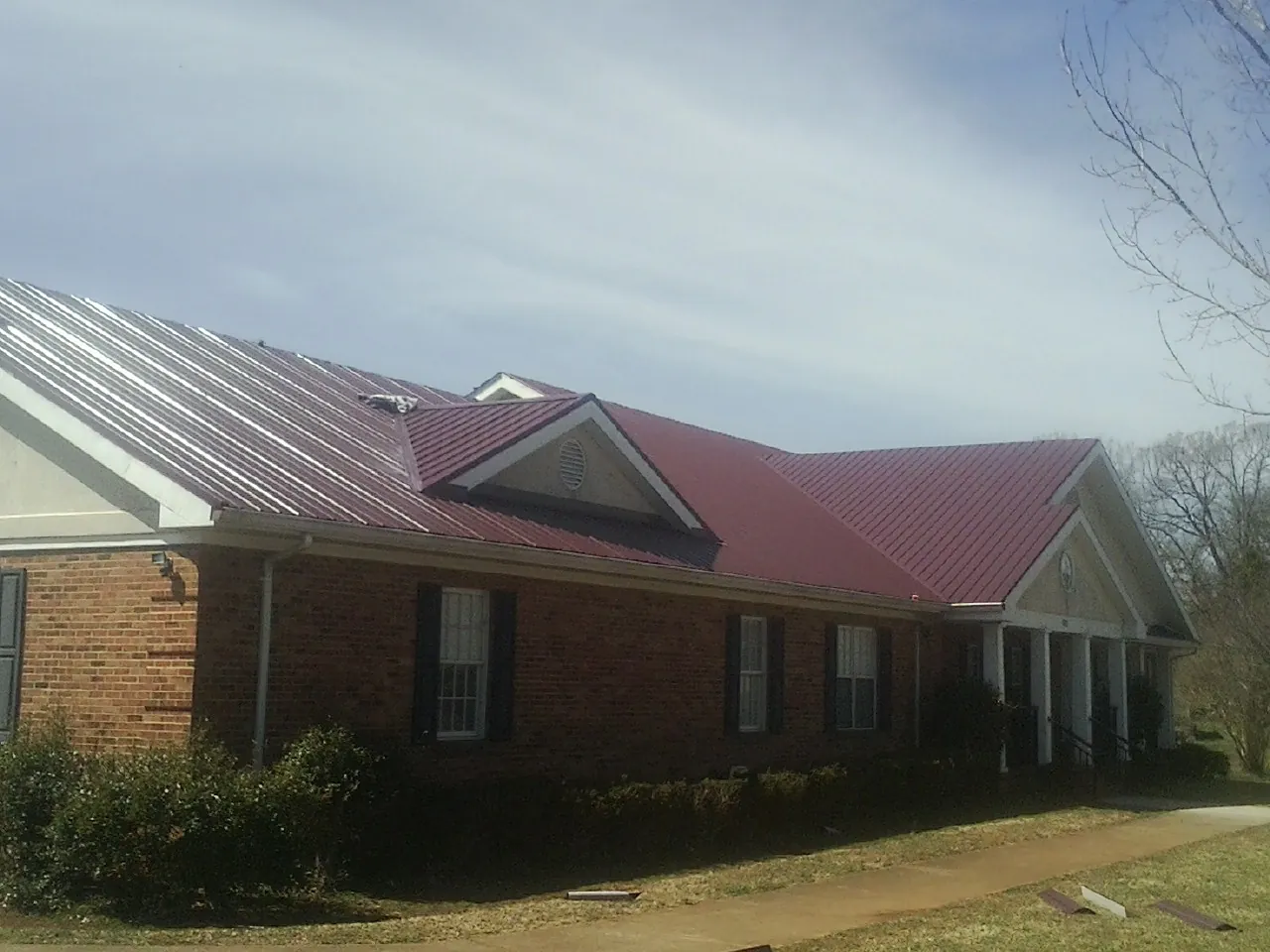 Red metal roof with gabled entries on a long brick building, from a Hail Damage Roof Repair job in Climax